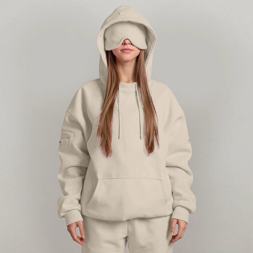 Person wearing a beige hoodie and pants with a matching eye mask on a gray background