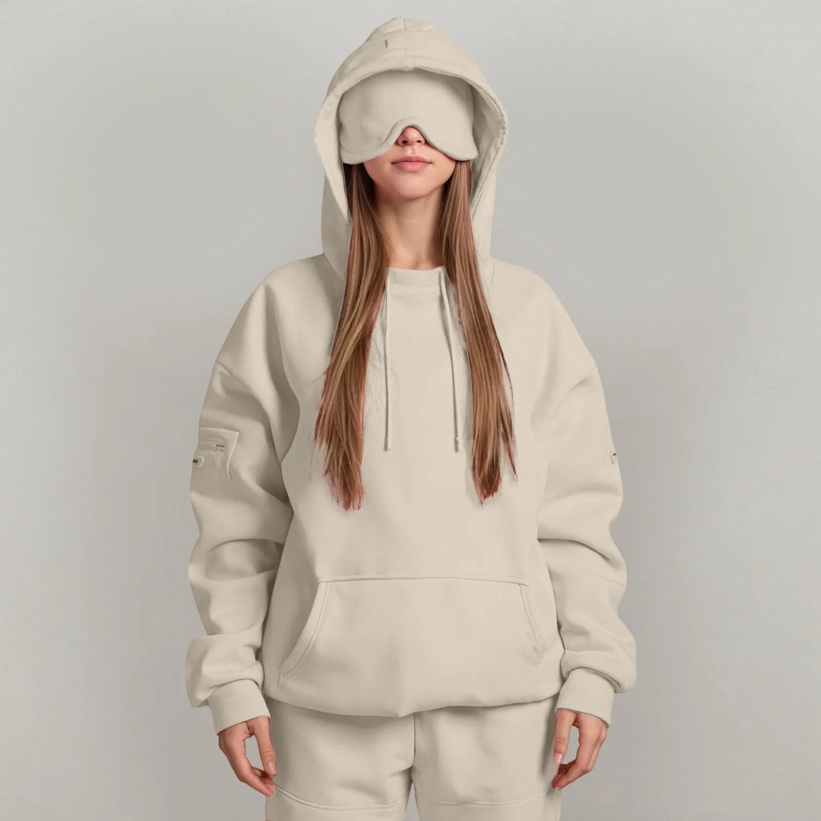 Person wearing a beige hoodie and pants with a matching eye mask on a gray background