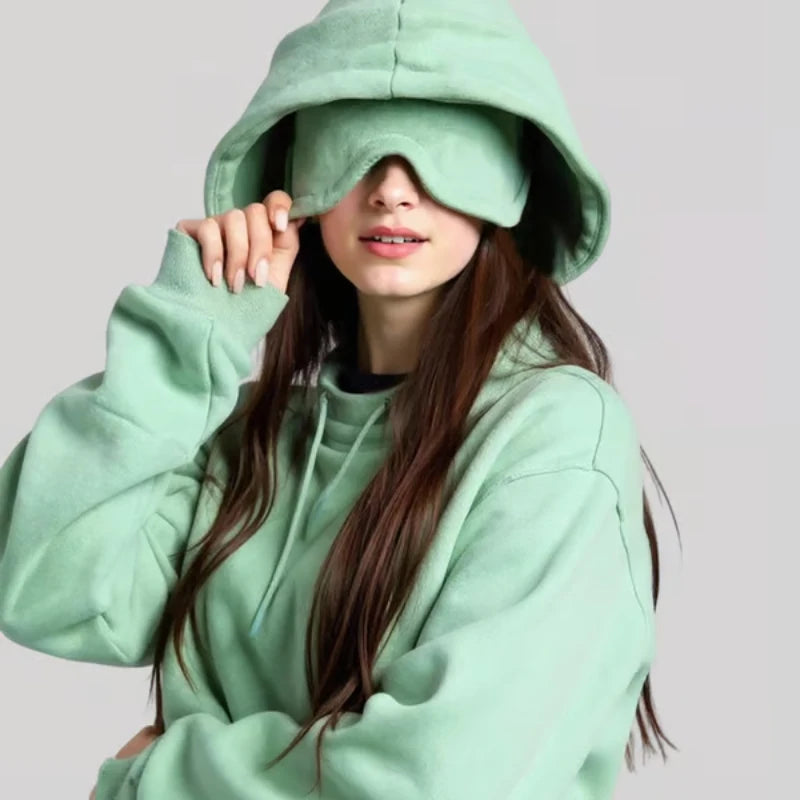 Person wearing a light green hoodie with the hood over their eyes on a plain background