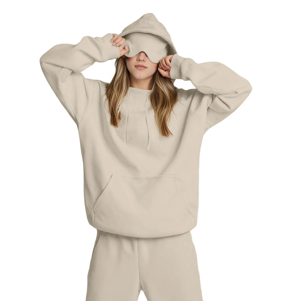 Person wearing a beige hoodie and matching pants with a sleep mask on a white background