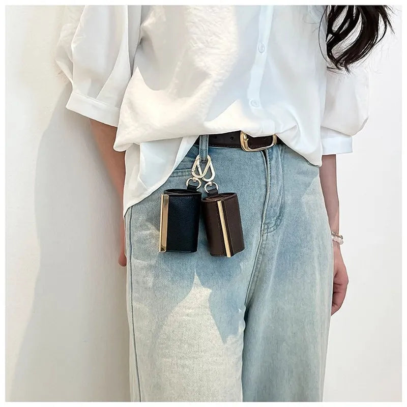 Person wearing a white shirt and light blue jeans with a black belt, holding two small rectangular objects.