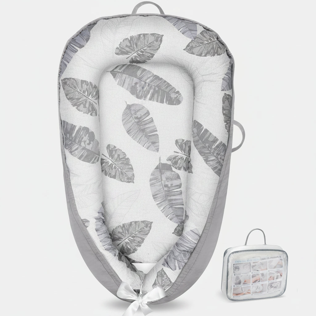 Baby lying in a gray and white leaf-patterned baby nest with a matching carrying case.