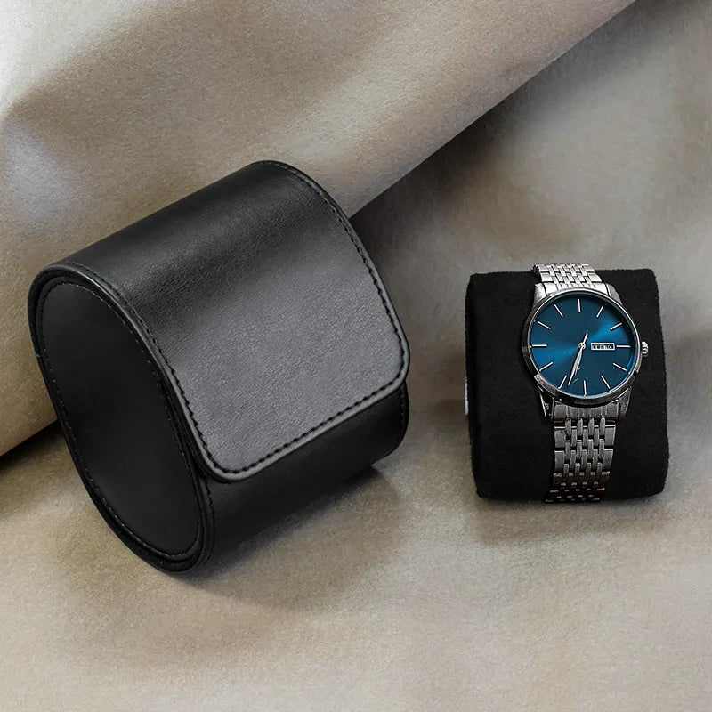 Watch with blue face and silver case on a black stand next to a black leather watch box on a beige surface.