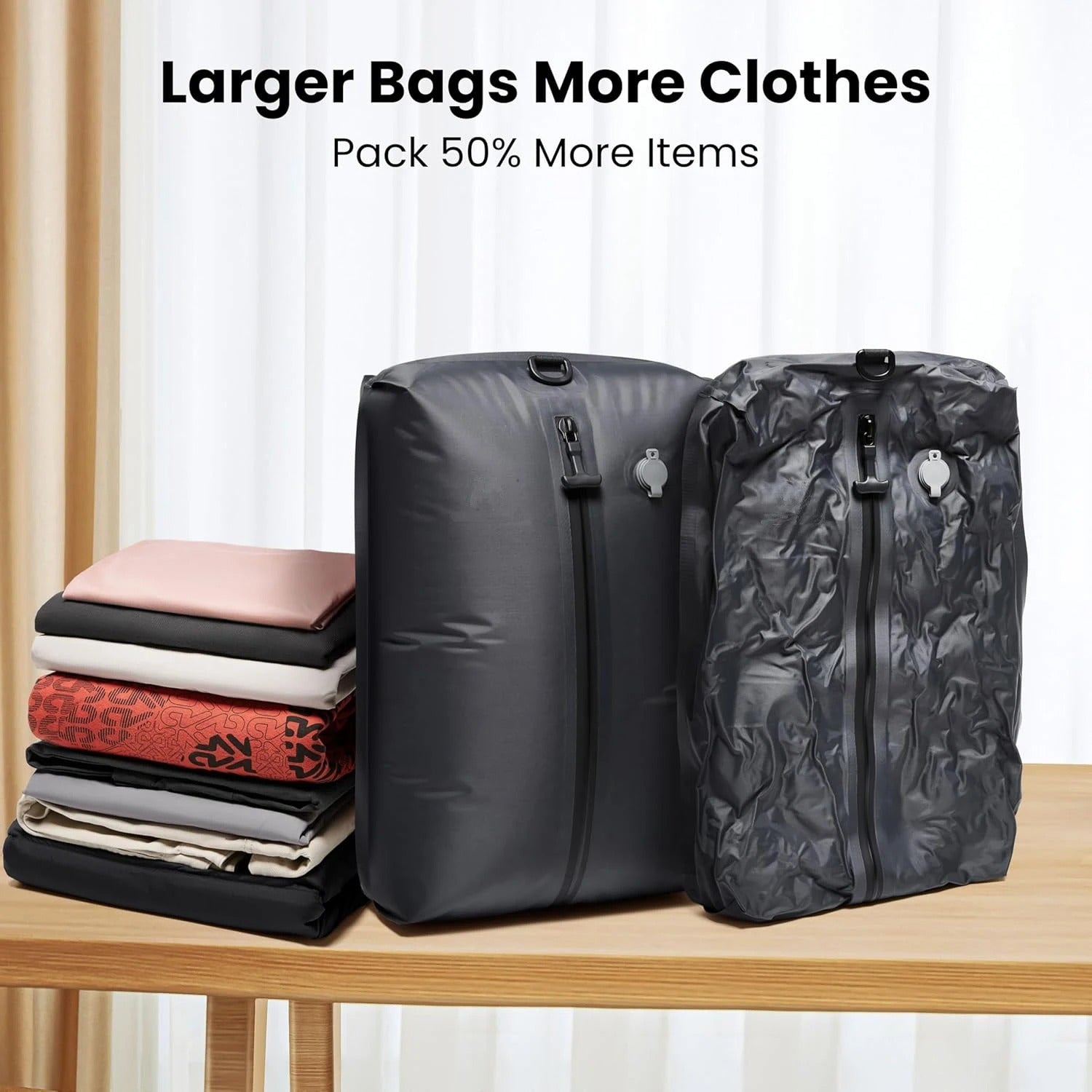 Two gray compression bags on a table with folded clothes beside them, against a white curtain background.