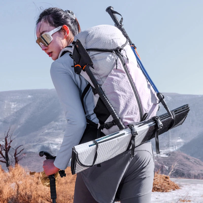 Person hiking with a large backpack and ski poles in a mountainous landscape