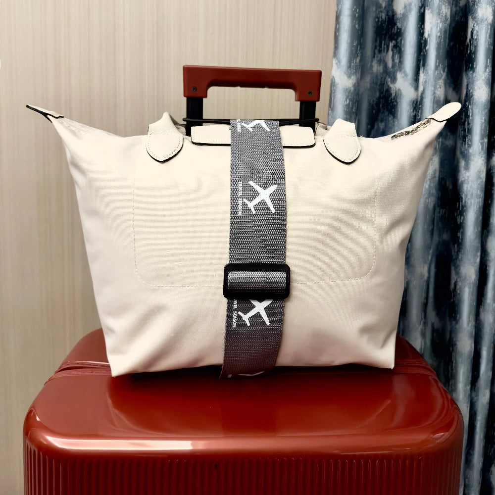 White travel bag with a gray strap featuring airplane icons on top of a red suitcase.