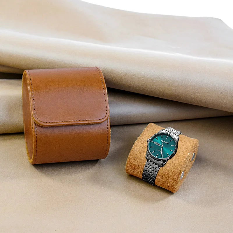 Brown leather watch case and green watch on a beige fabric background
